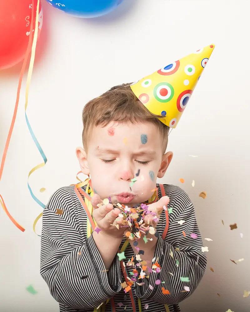 Junge mit Partyhut bläst Confetti in die Luft